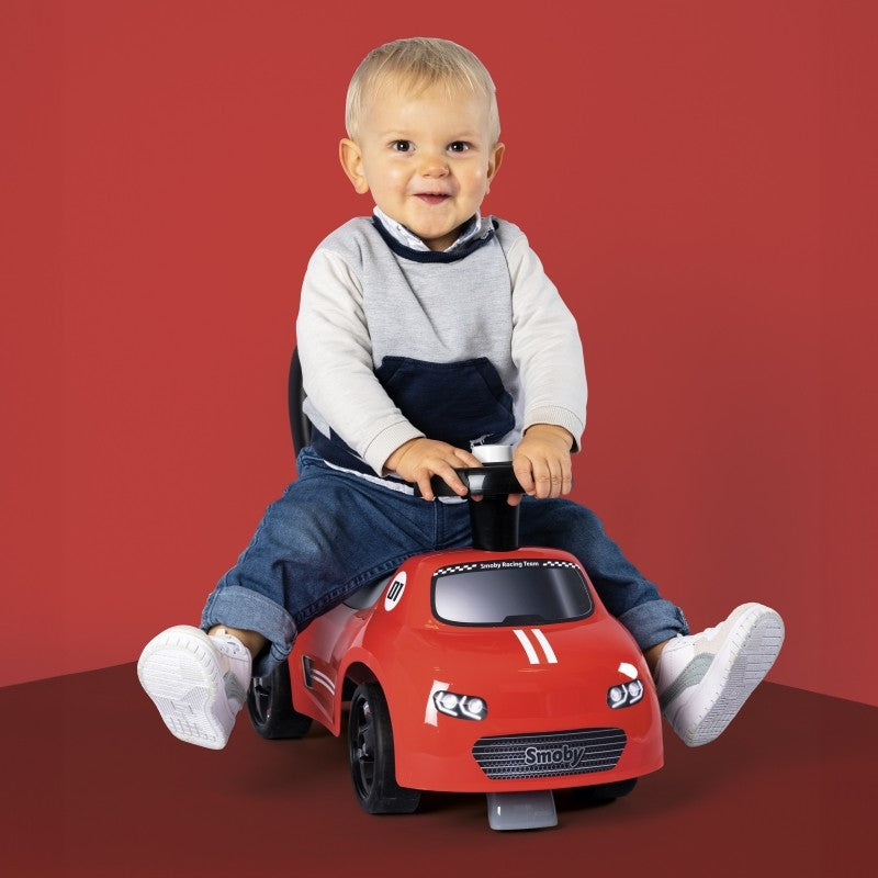 Baby riding red Smoby car demonstrating stable posture and ergonomic design for ages 10m+