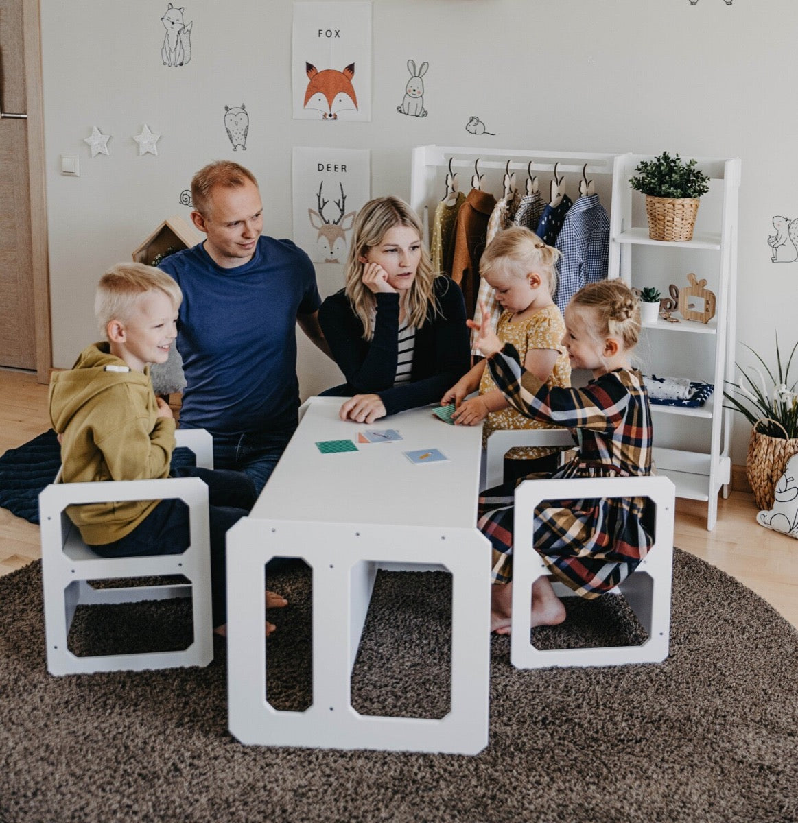 Family of five gathered around white Montessori table and chairs set in living room during group activity