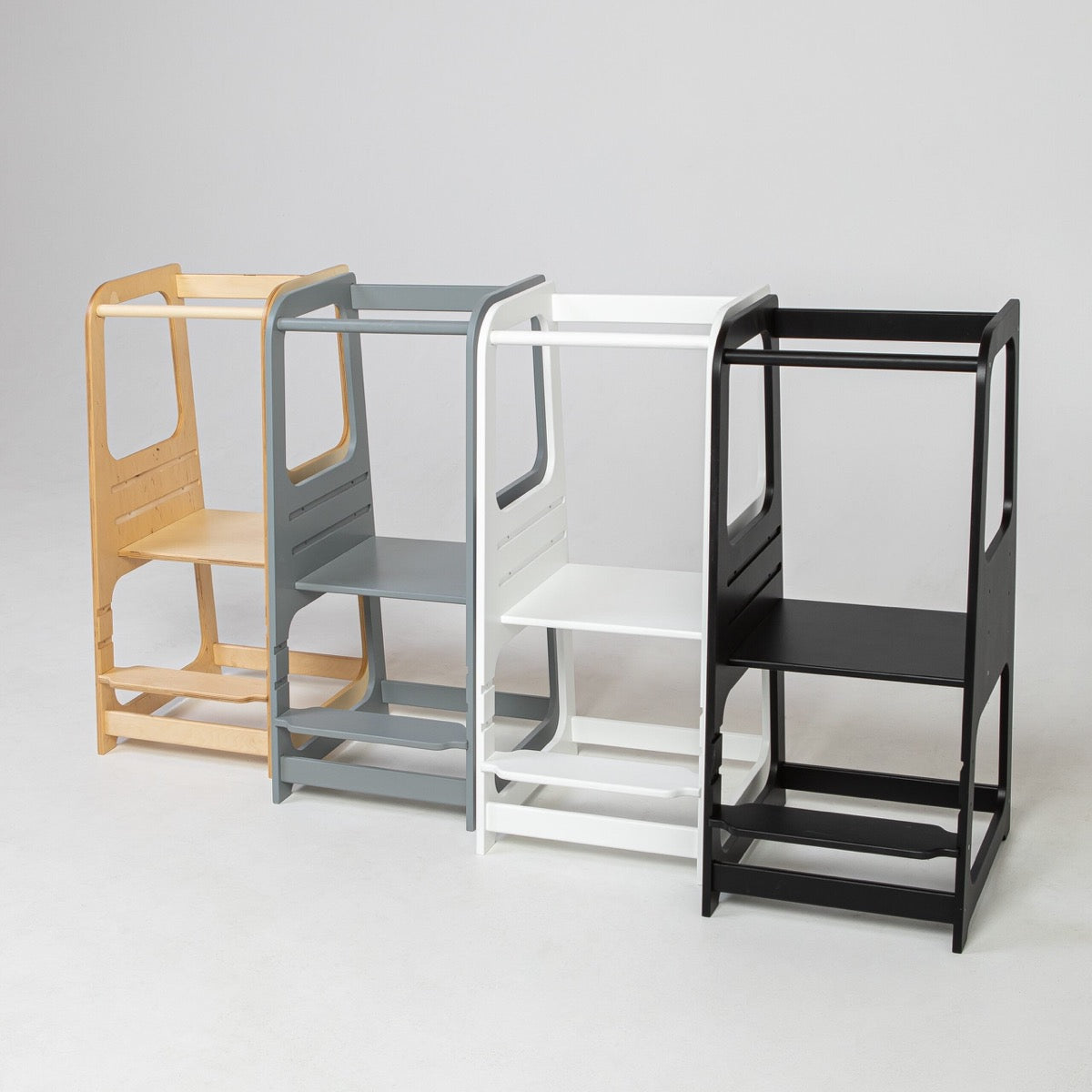 Four Montessori helper towers displayed in natural wood, gray, white, and black finishes