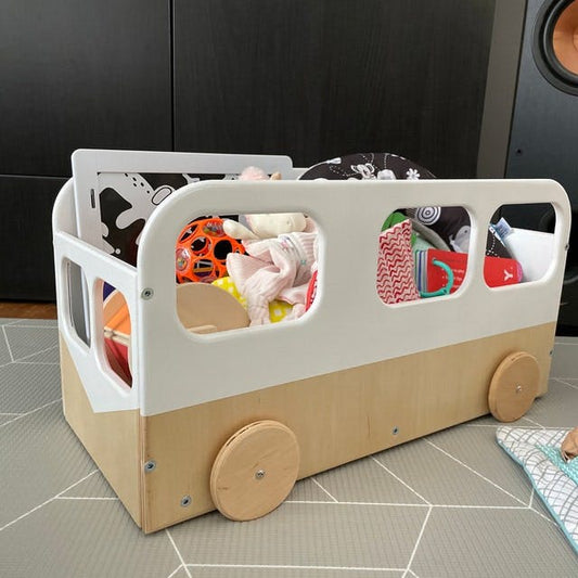 Wooden bus-shaped toy storage box filled with toys and clothes, showing visible compartments and wooden wheels