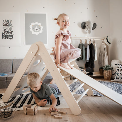 Two toddlers playing on wooden climbing triangle with ramp in modern Montessori bedroom