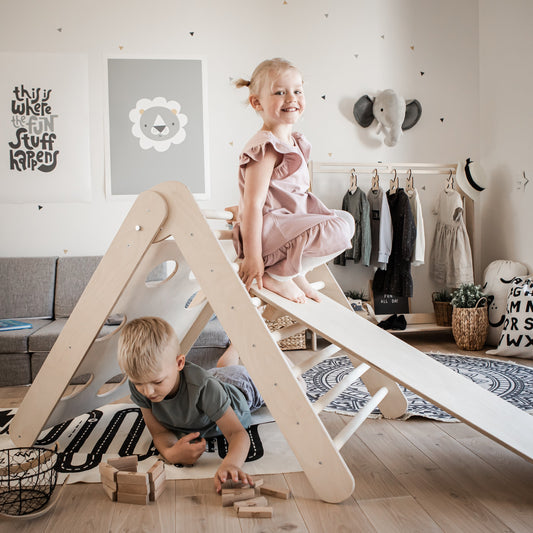 Two toddlers playing on wooden climbing triangle with ramp in modern Montessori bedroom
