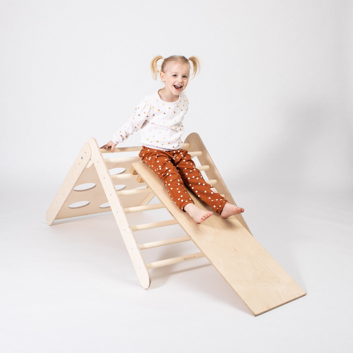 Young child sliding down ramp of wooden 2-in-1 climbing triangle with ladder