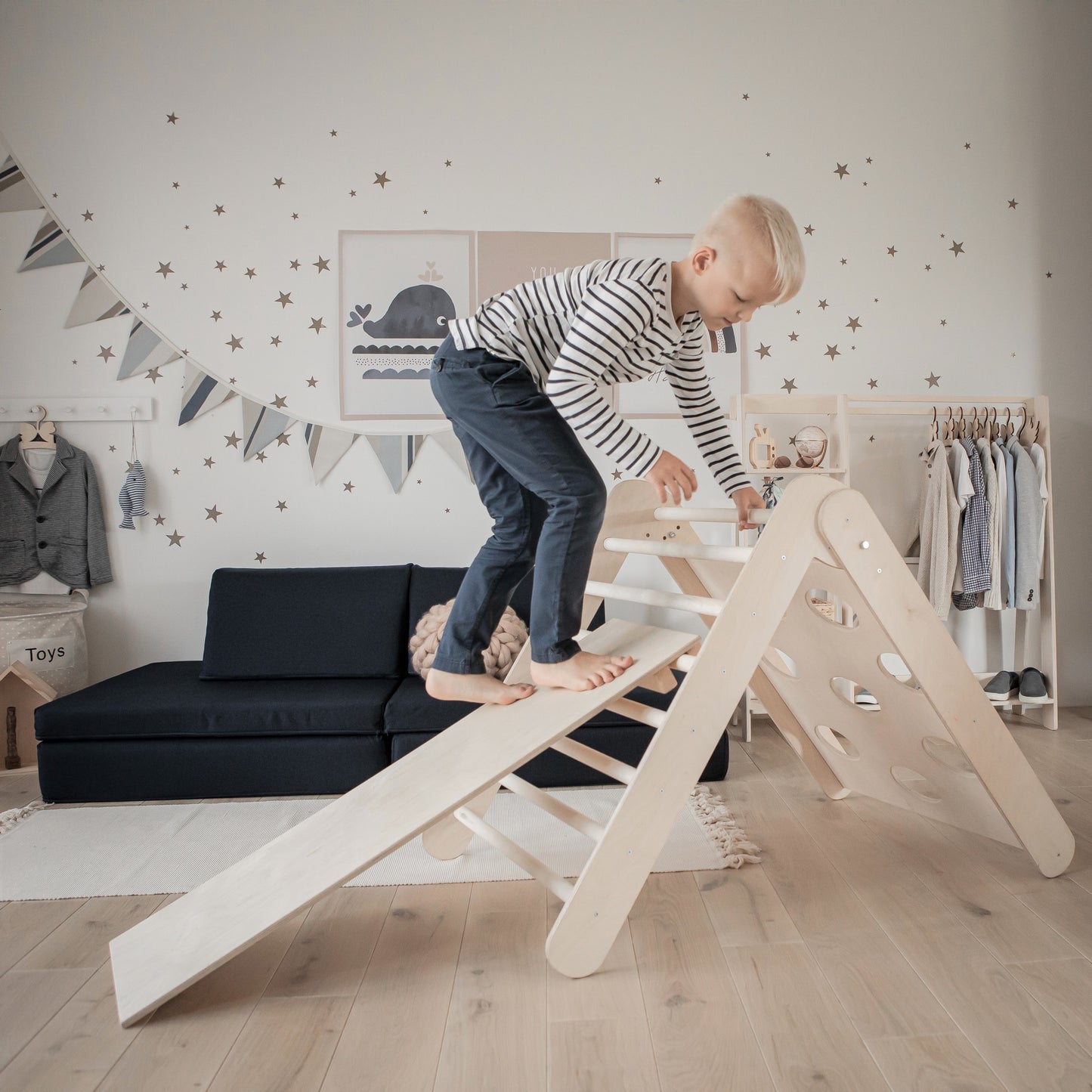 Boy climbing rungs of wooden triangle while girl slides down ramp in bedroom