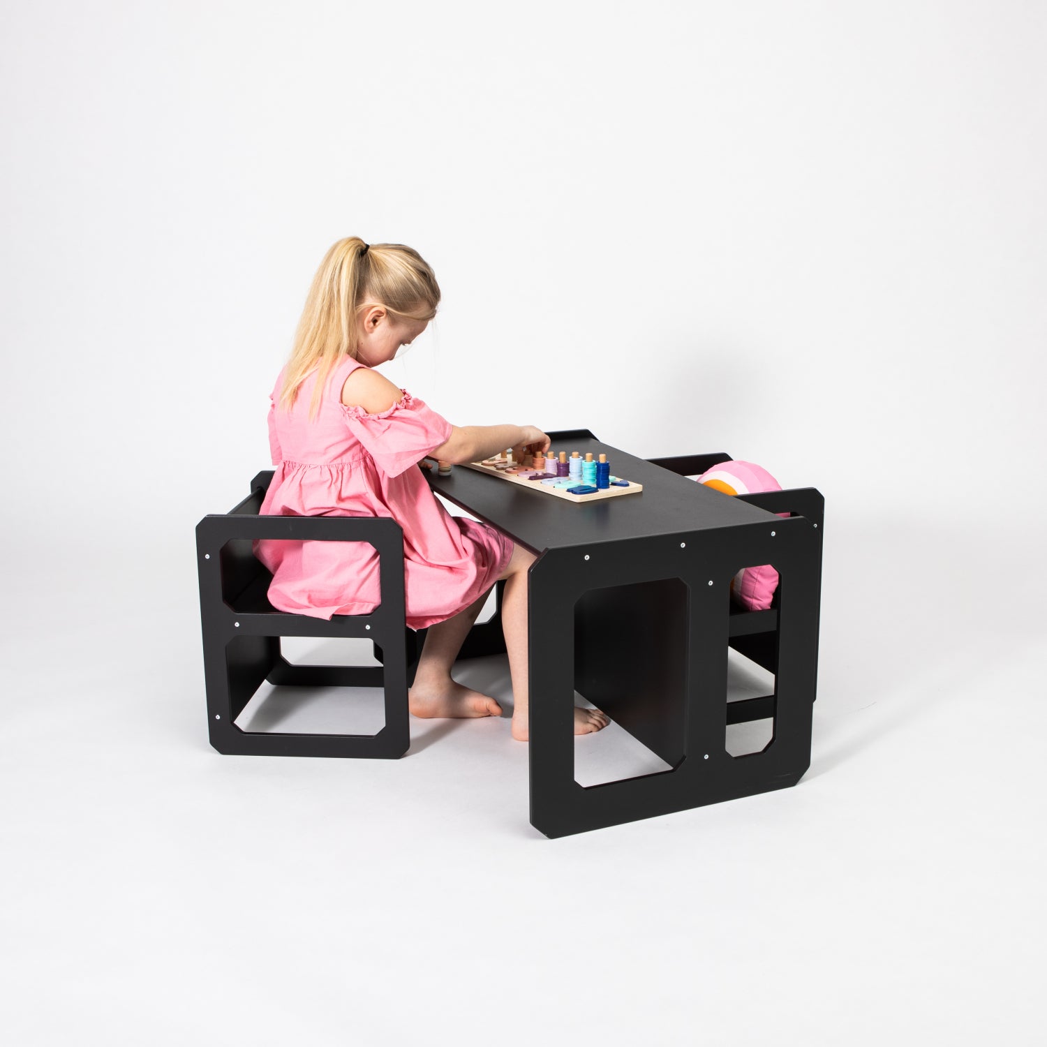 Child in pink dress seated at black Montessori table and chair set playing with toys