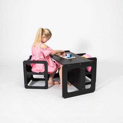 Child in pink dress seated at black Montessori table and chair set playing with toys