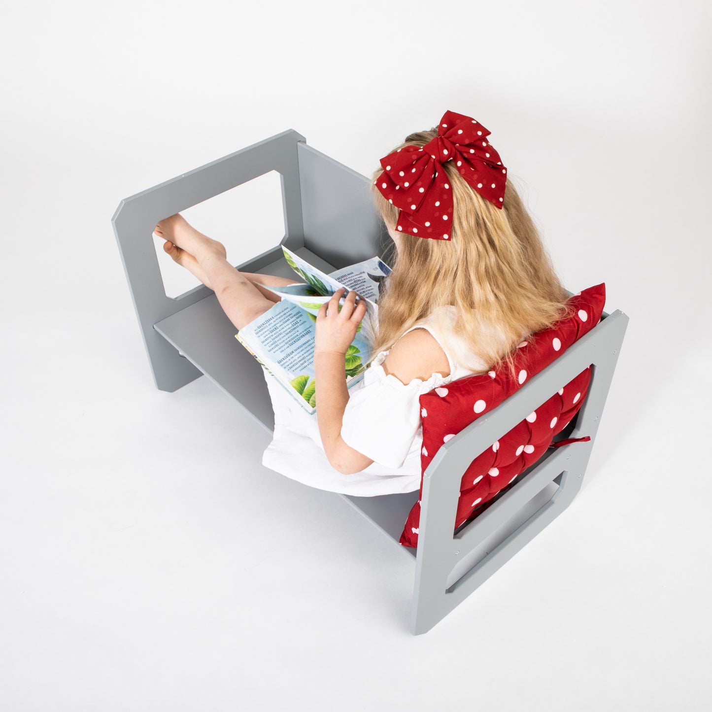 Toddler girl sitting at gray Montessori table reading book independently
