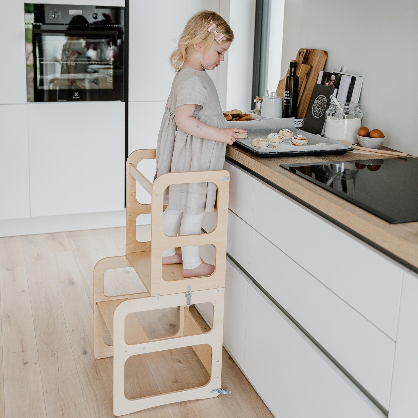 Child using natural wood kitchen tower step stool at adult kitchen counter