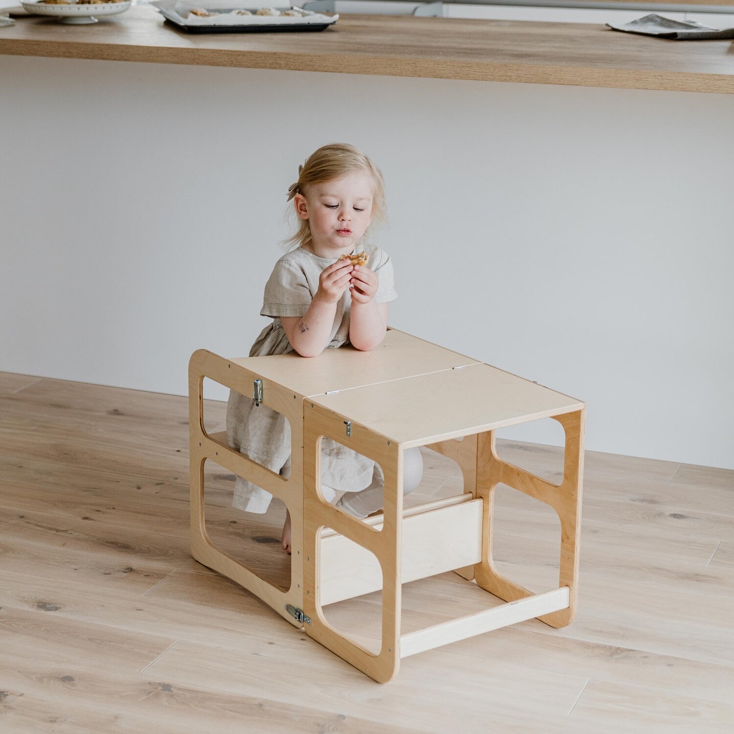 Young child seated at natural wood Montessori kitchen tower table in dining position