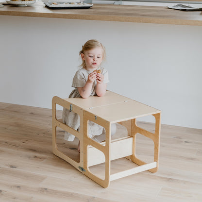 Young child seated at natural wood Montessori kitchen tower table in dining position