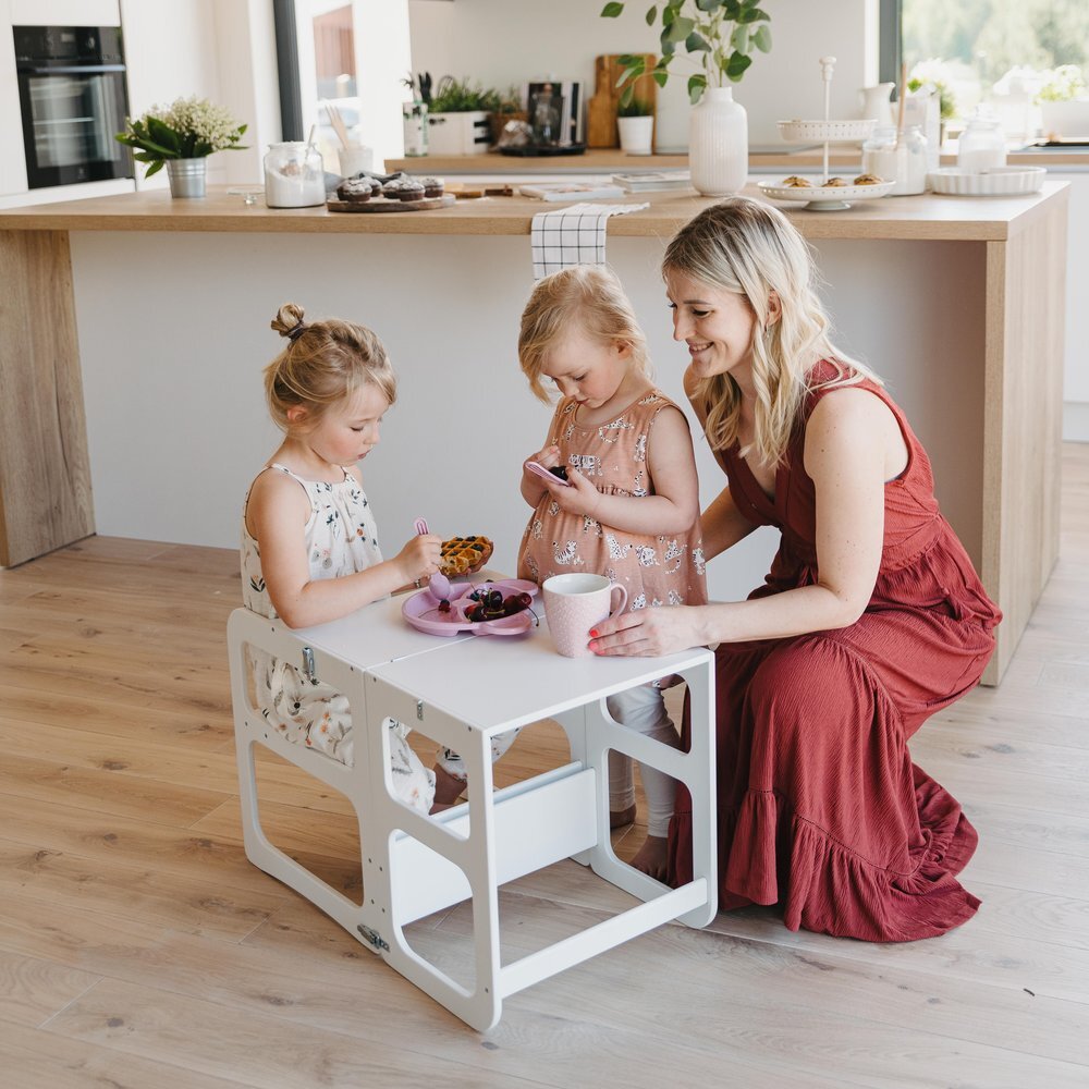 Adult and toddlers gathered around white kitchen tower table for snack time