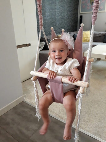 Toddler sitting in dusty pink crown-shaped velvet swing with wooden bar and rope hanging