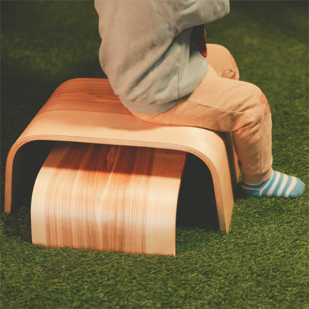 Child stepping on single wooden step stool on grass outdoors