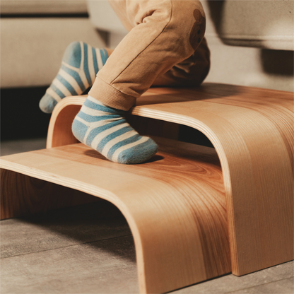 Close-up of child's feet on wooden step stool with curved design