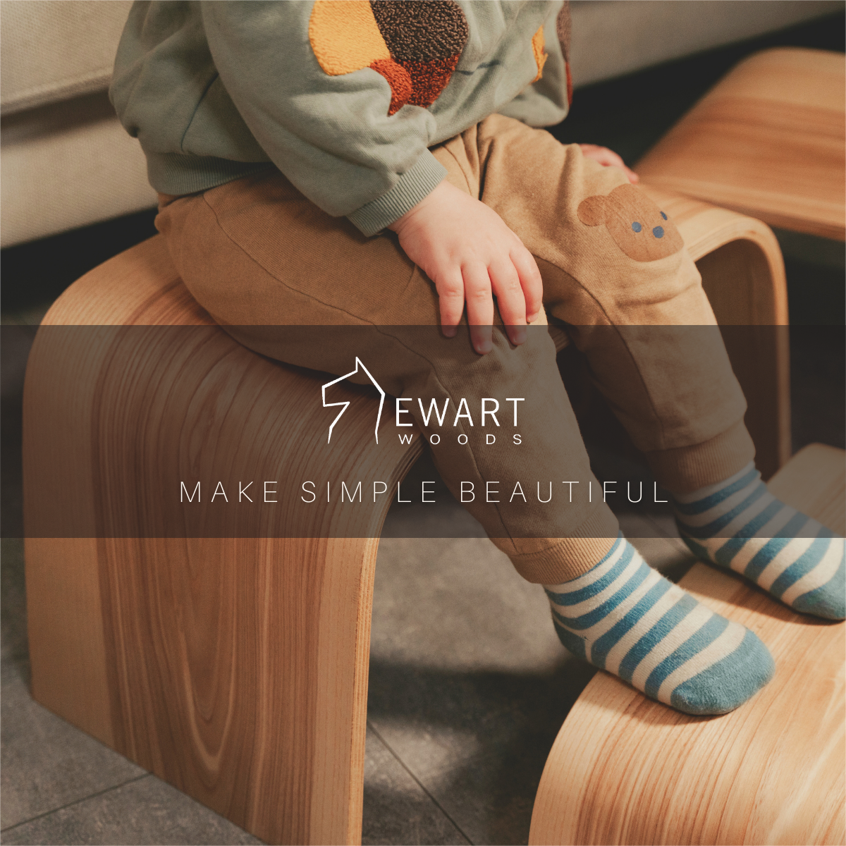 Young child sitting on stacked wooden step stools with Ewart Woods branding