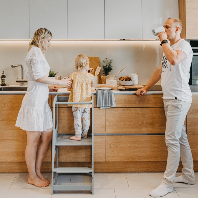Family of three cooking together with child elevated on gray helper tower stool