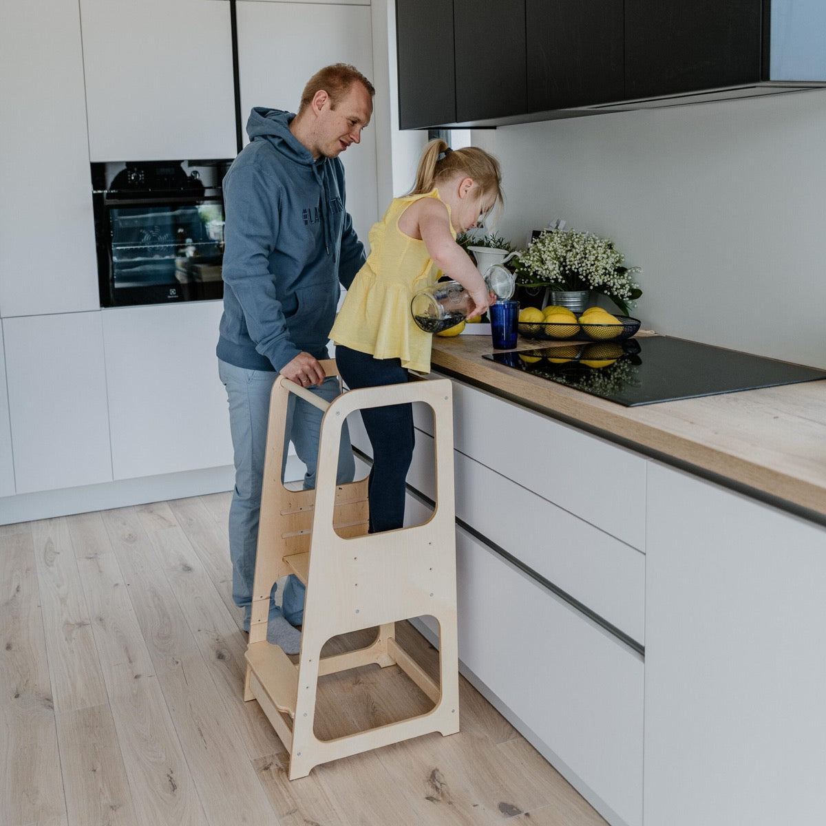 Child reaching counter with assistance while standing on natural finish helper tower