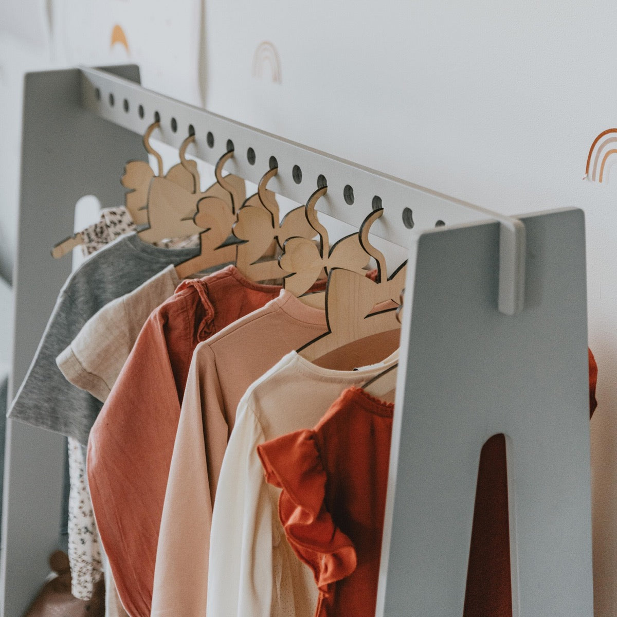 Close-up of wooden hangers holding colorful children's outfits on grey clothing rack