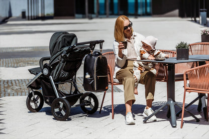 Woman seated with stroller wearing espresso diaper backpack hands-free