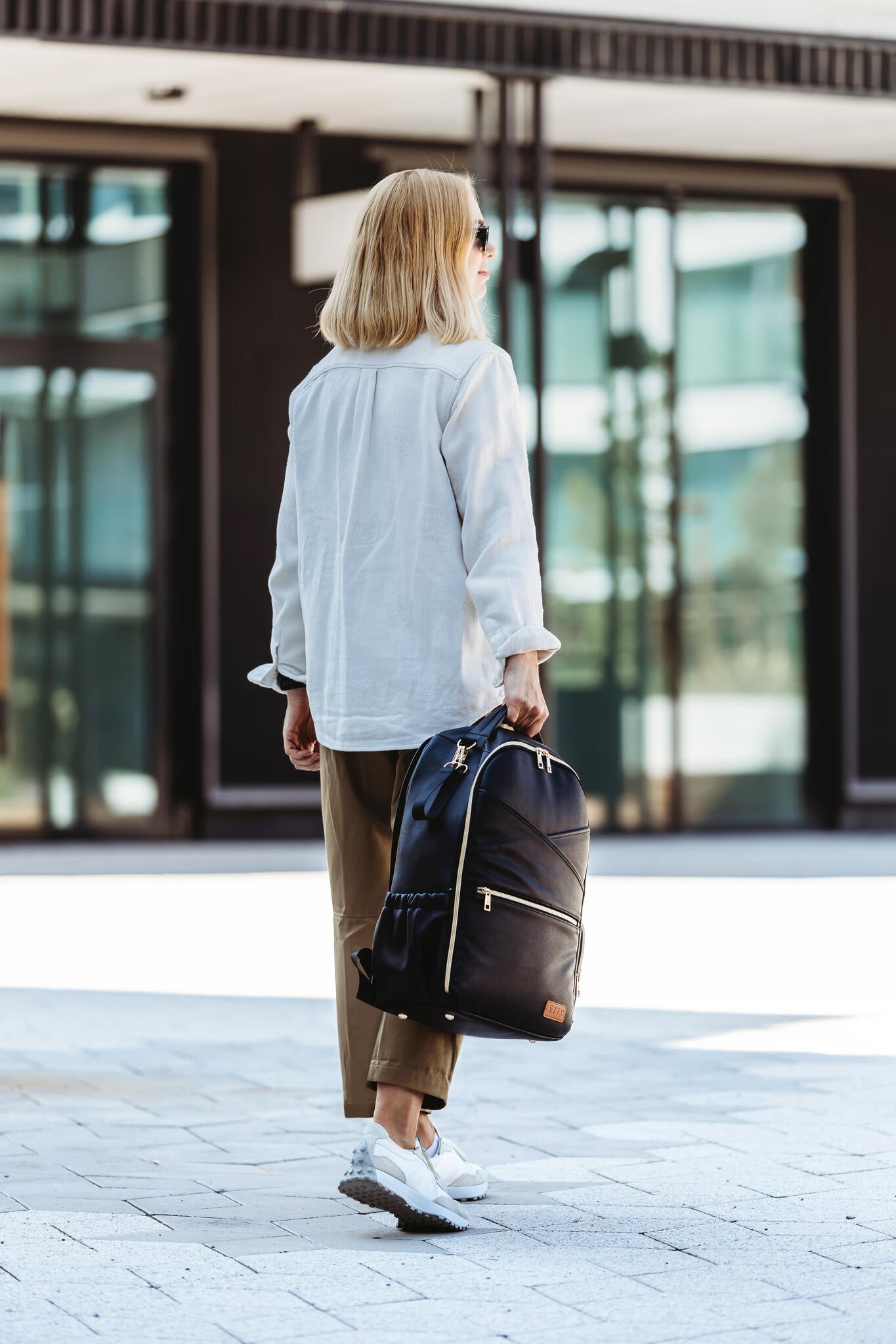 Woman from behind carrying espresso diaper backpack while walking