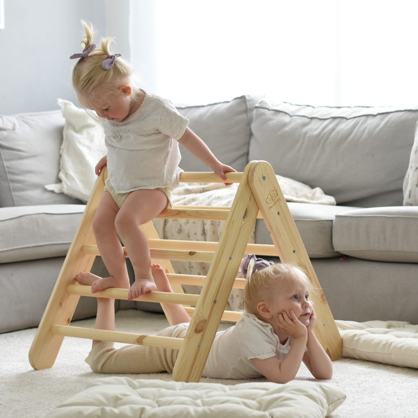 Two children using natural wood ladder climbing structure with pink tent