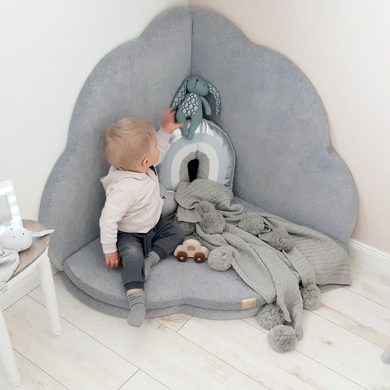 Toddler sitting inside grey cloud shaped play mat surrounded by toys and blankets