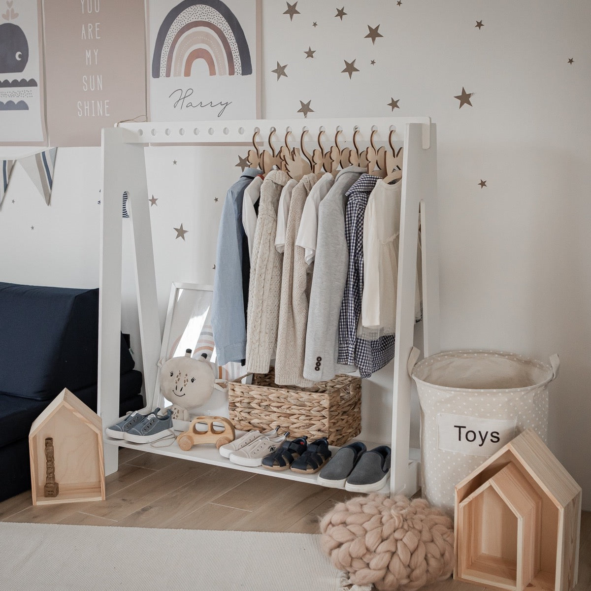 White dress-up rack in nursery corner with pink and neutral toddler clothing organized