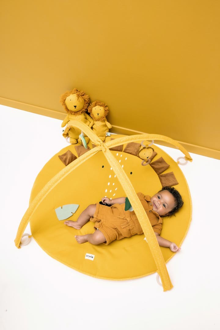 Baby lying on Mr. Lion activity mat surrounded by hanging teethers and sensory toys