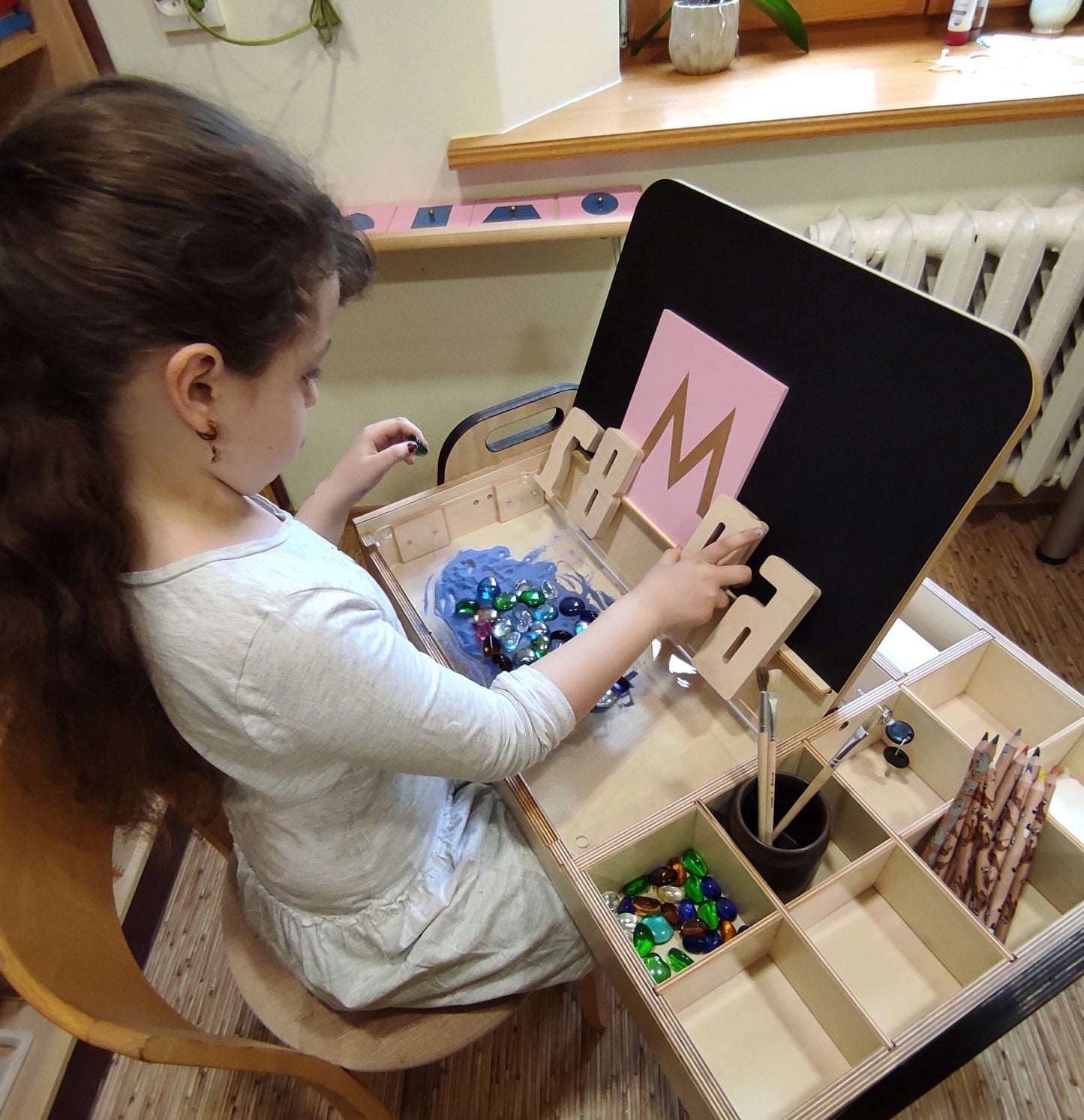Girl organizing craft supplies in compartmentalized storage drawers of Montessori table