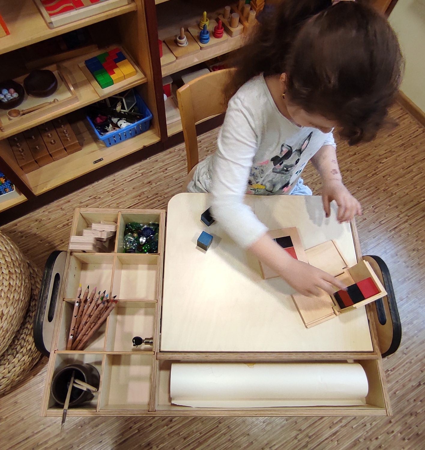 Overhead view of child using paper roll and organized supplies at Montessori table