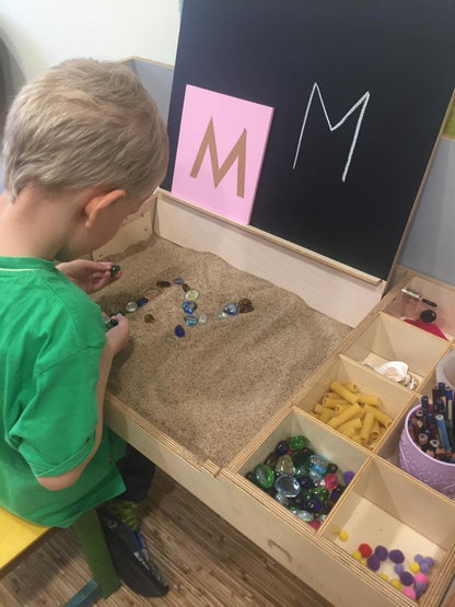 Child using sensory play materials in compartments of Montessori table for focused learning