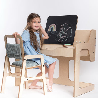 Child sitting at mint green Montessori table and chair set, drawing on blackboard