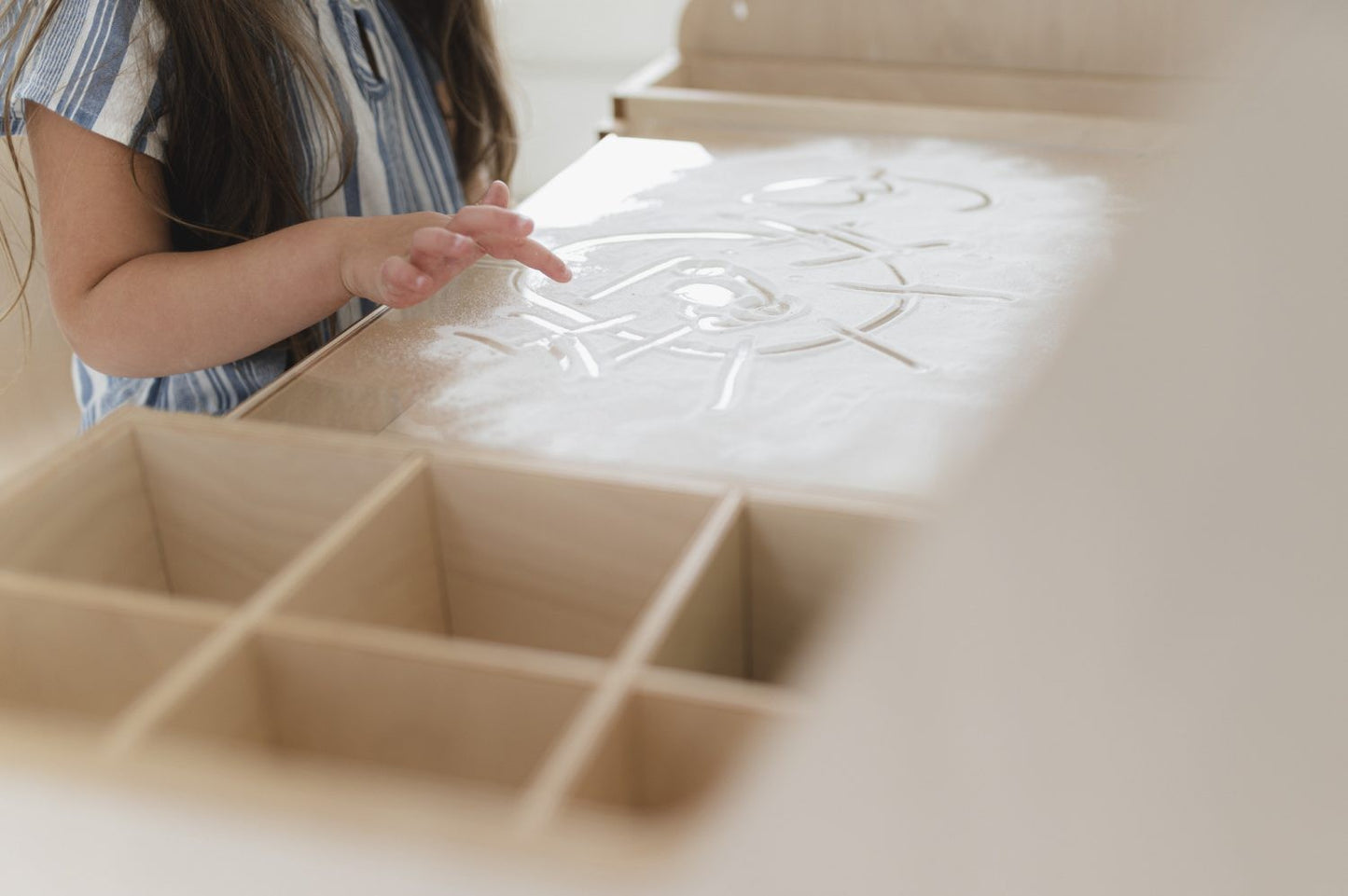Child's hand sketching on white laminated surface of adjustable Montessori table during drawing activity