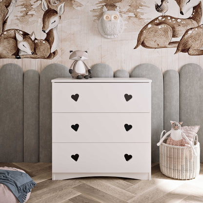 White three-drawer chest with heart cutout handles against upholstered headboard