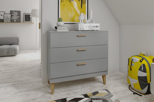 Grey Kubi chest of drawers with oak legs in minimalist nursery setting with decor on top