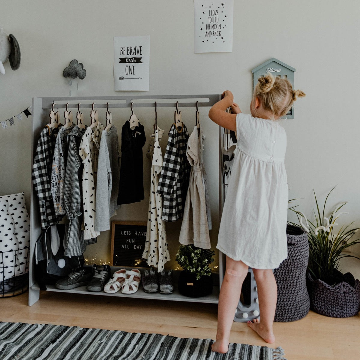 Grey kids clothing rack displaying patterned clothes and shoes, child reaching for garments