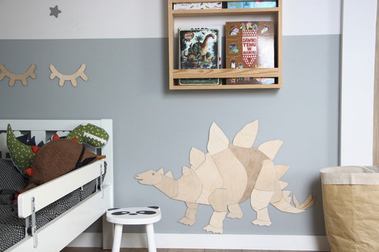 Wooden stegosaurus wall decoration mounted on blue nursery wall above white stool