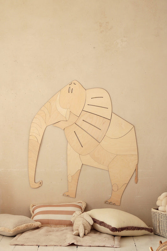 Wooden elephant wall decoration mounted on beige wall above cushions and toys in nursery