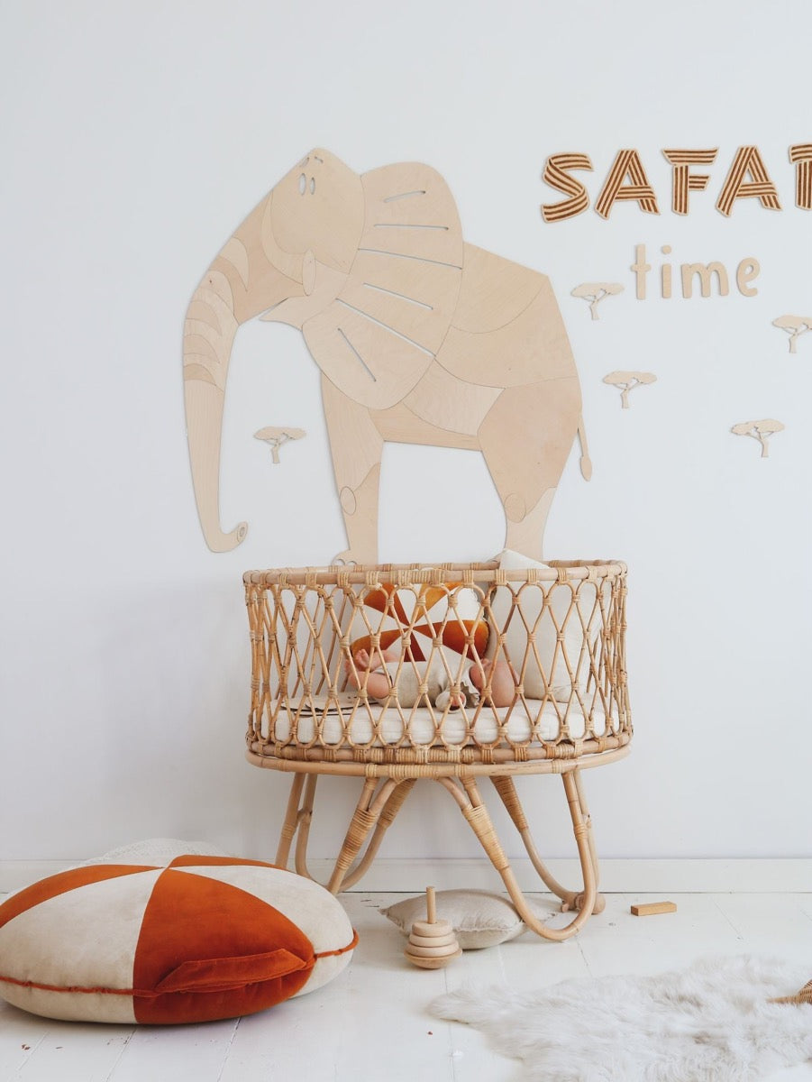 Large wooden elephant wall decor positioned above wicker bassinet in playroom display