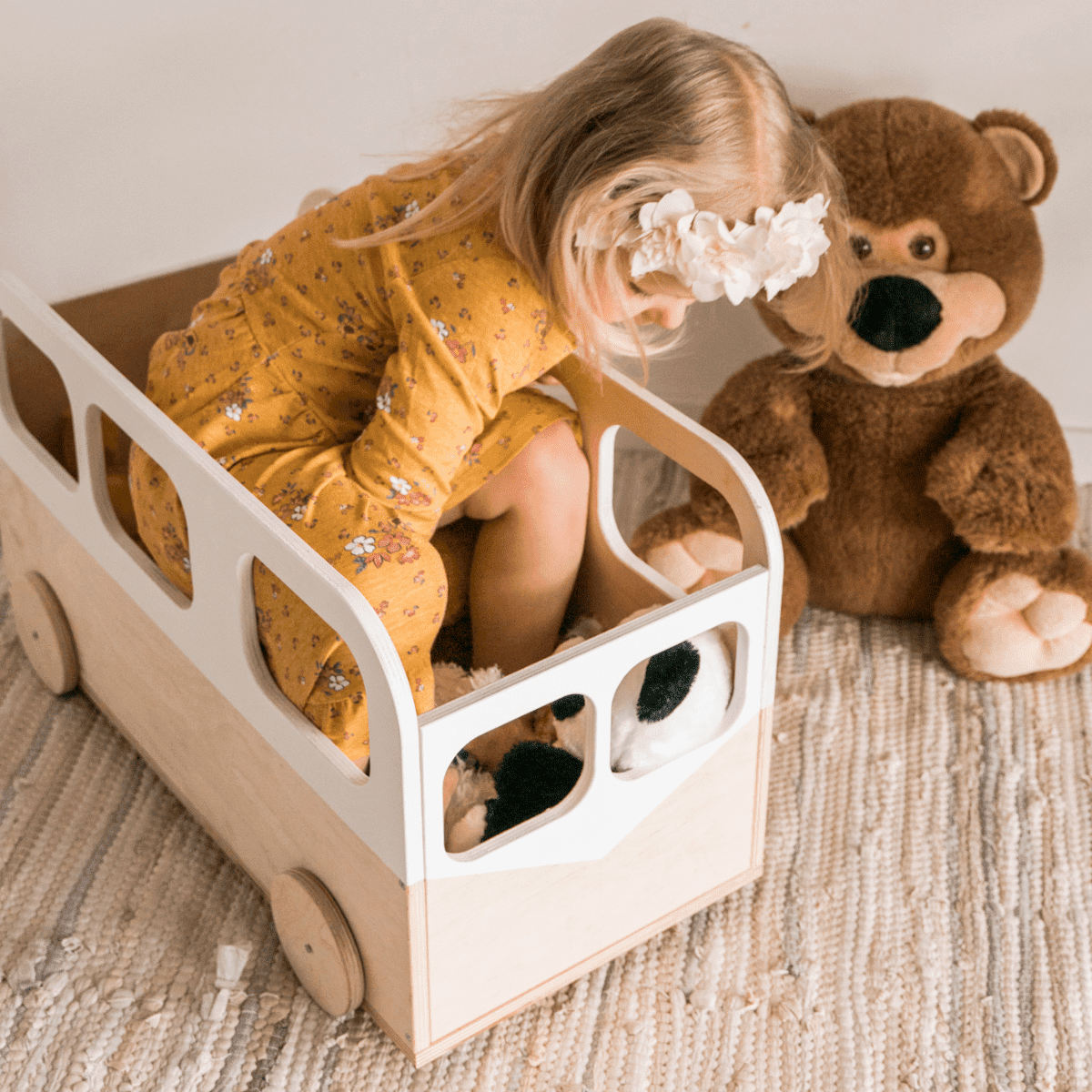 Child playing in wooden bus toy storage box with stuffed animals and toys inside