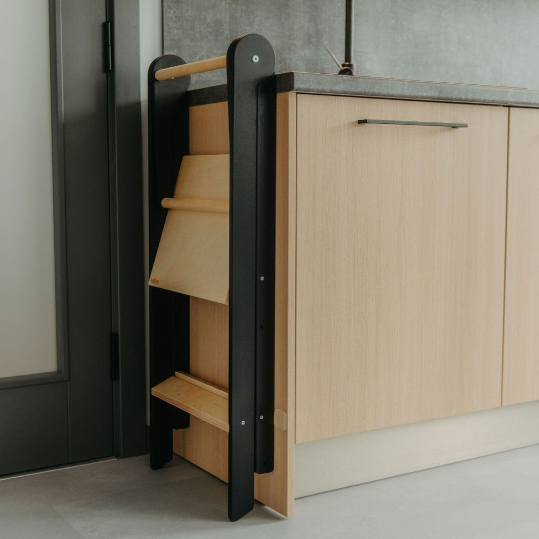 Folded kitchen tower with black frame and natural wood steps stored compactly next to kitchen cabinet