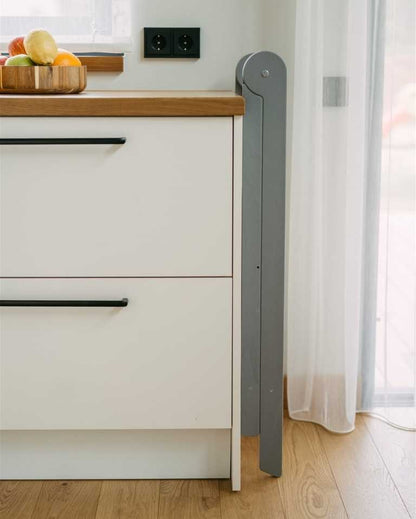 Toddler playing at table while standing on folded natural wood kitchen tower with safety rail visible