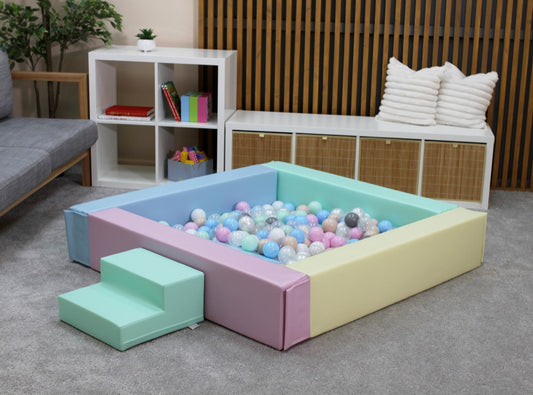 Light pastel foam ball pit with low-profile entrance filled with colorful soft play balls in an indoor playroom