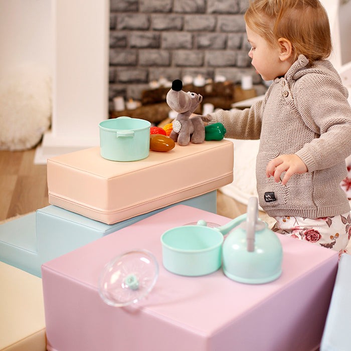 Toddler using pastel foam blocks as stepping stones with toys on top