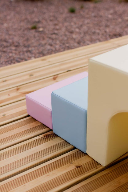 Detail shot of pastel pink and blue foam blocks stacked on wooden surface