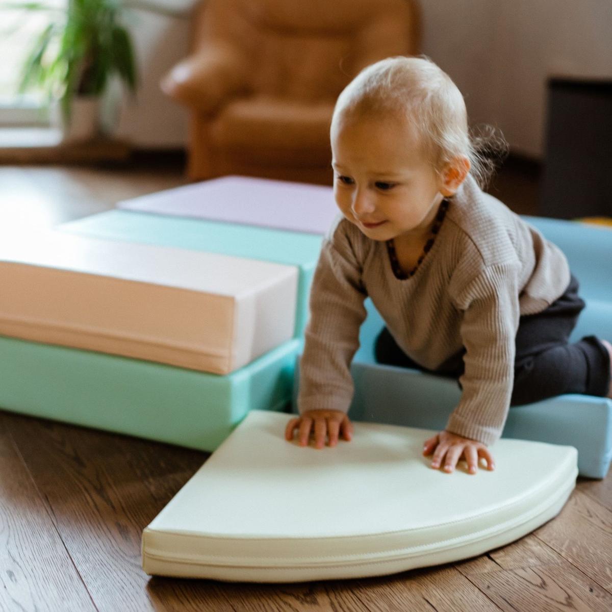 Toddler crawling on light pastel foam oval mat and blocks in play setup
