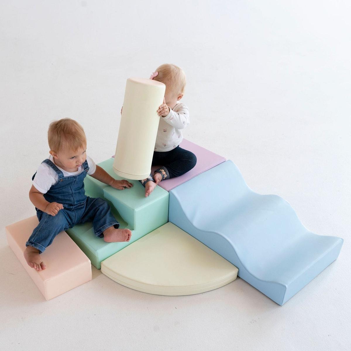 Two toddlers playing on light pastel foam blocks arranged as climbing structure