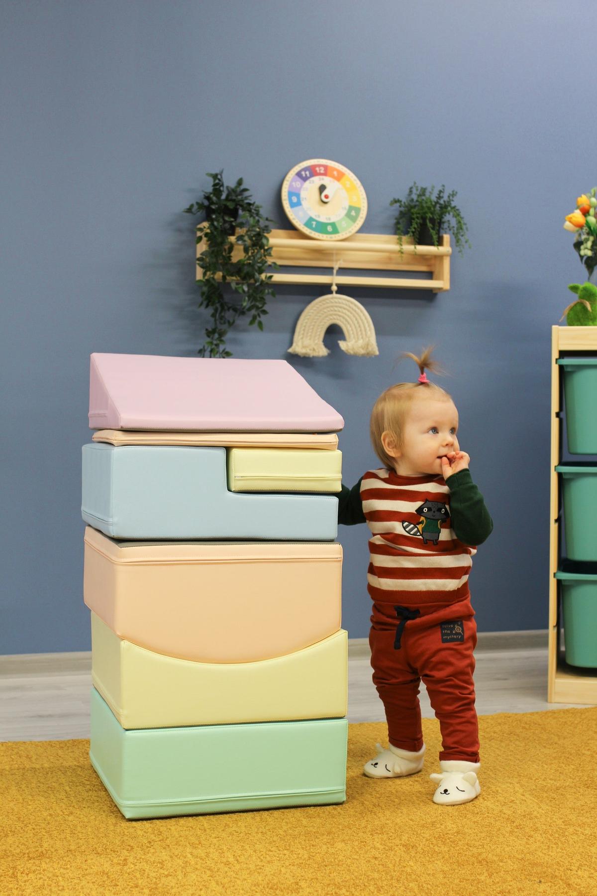 Toddler playing beside tall stack of soft pastel foam blocks for climbing