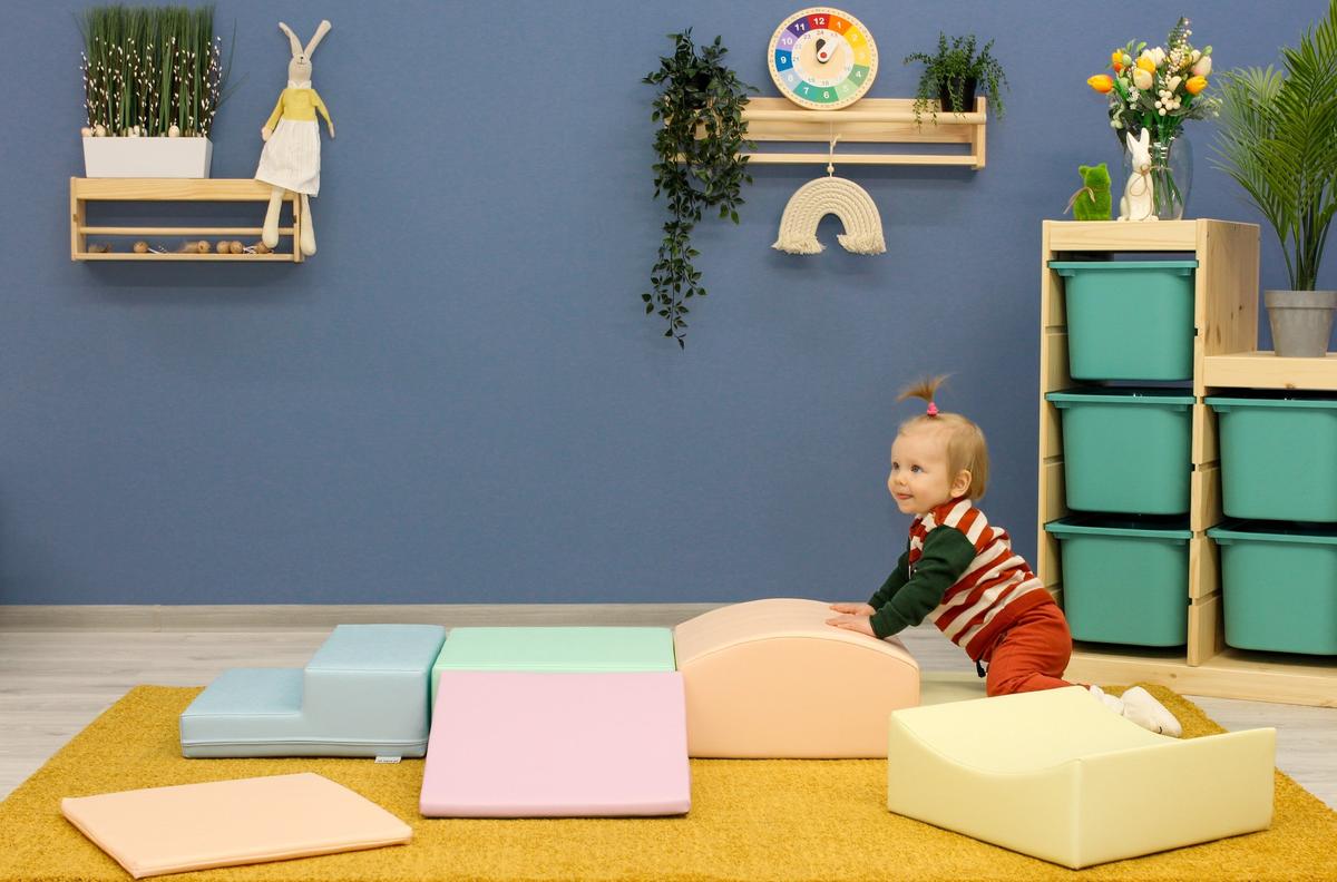 Child exploring pastel foam climbing blocks spread across playroom floor