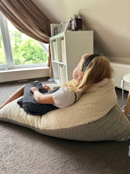 Child resting against cream and gray sherpa bean bag in bedroom